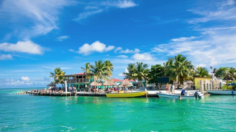 Lively waterfront with a pier, boats, and a two-story tropical building.