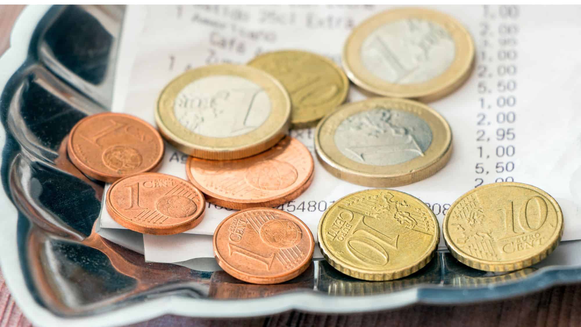 A small silver tray holds several euro coins alongside a restaurant receipt, indicating a tip left for service.