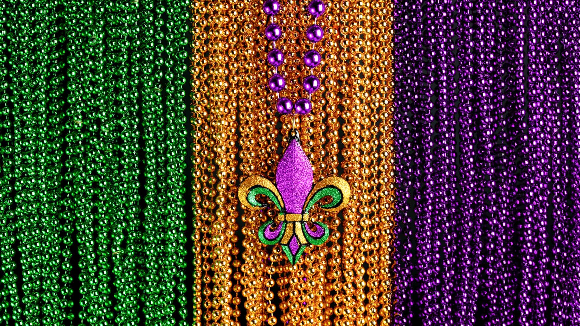 Close-up of vibrant Mardi Gras beads in green, gold, and purple, with a glittery fleur-de-lis pendant at the center.