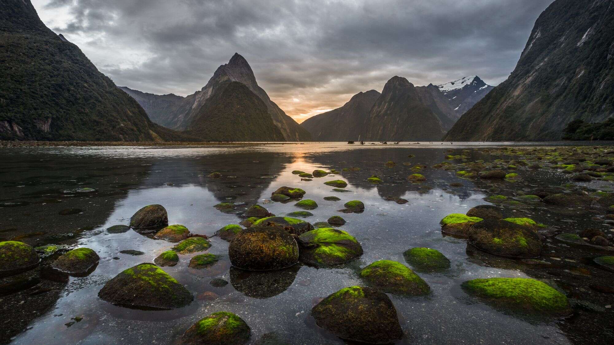 Milford Sound under a partly cloudy sky at a lake showing the mountains in the water reflection.