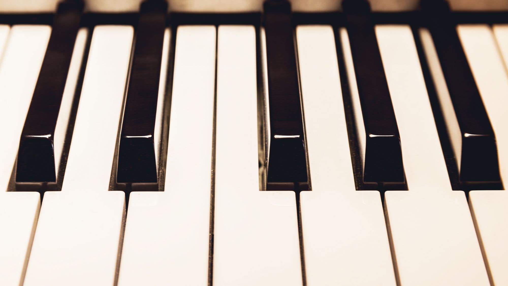 A detailed close-up of black and white piano keys, highlighting their glossy texture. The perspective gives a sense of depth and symmetry.