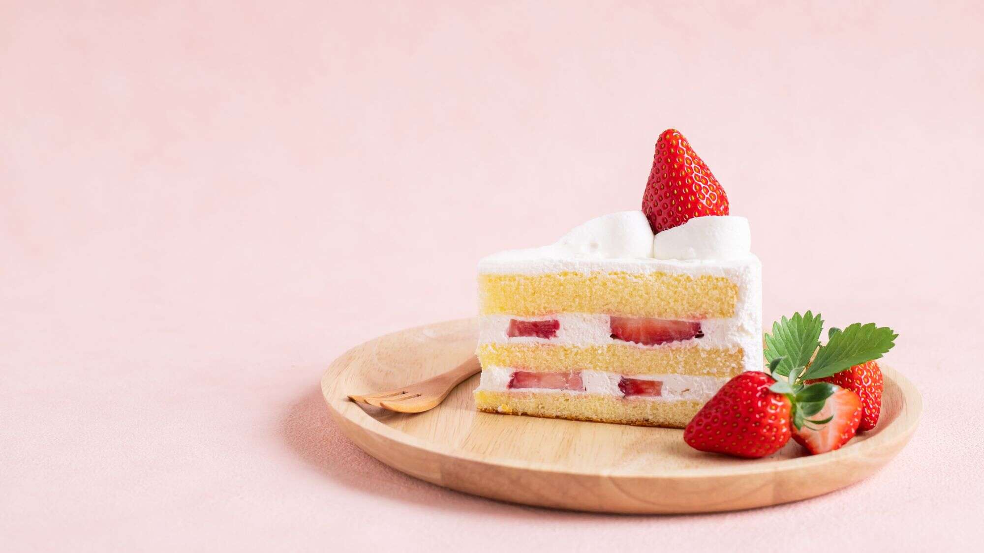 A plate of classic strawberry shortcake served with a several strawberries on a small wooden plate.