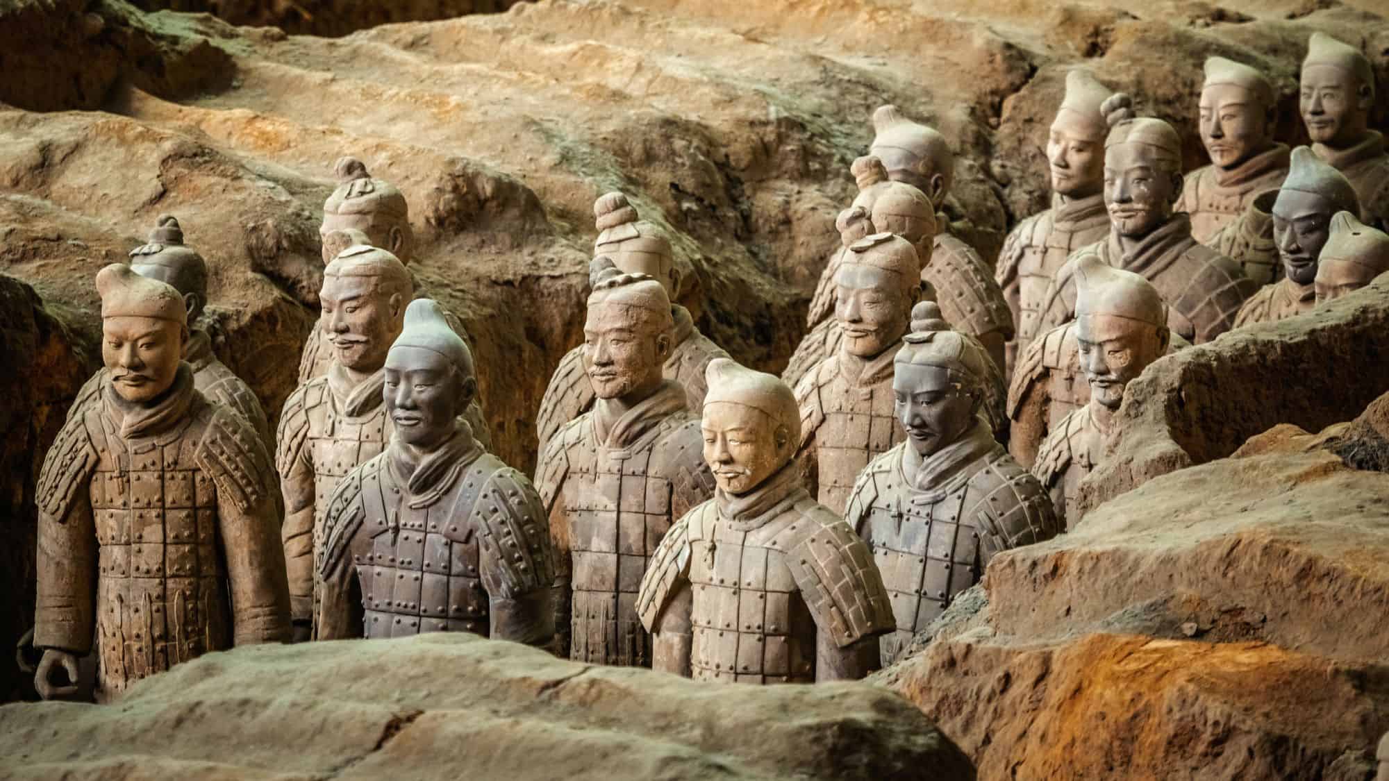 A close-up view of the Terracotta Army, depicting rows of life-sized clay soldiers with detailed armor and expressions. The warriors, buried with China's first emperor Qin Shi Huang, stand in formation in their underground tomb.