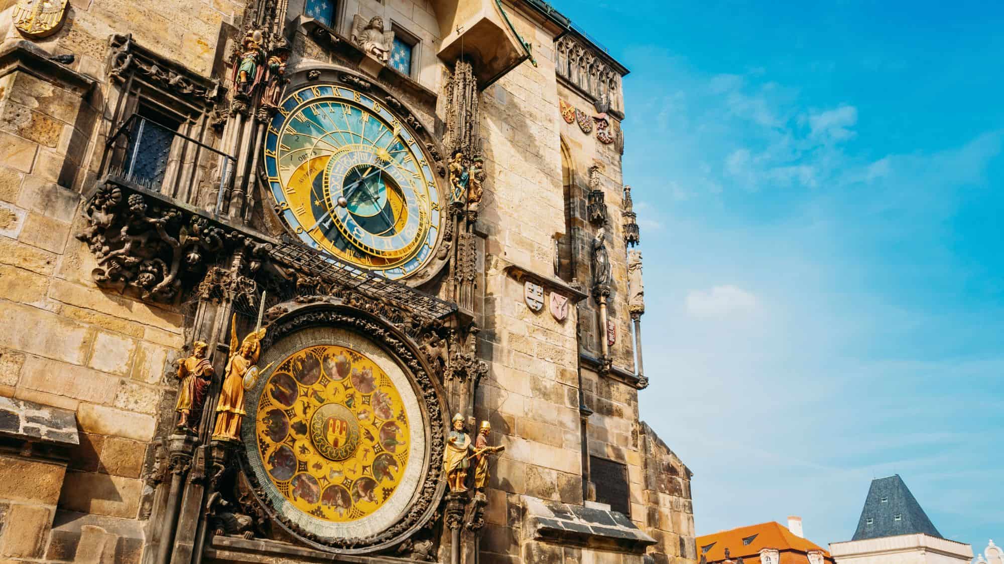 A close-up of Prague’s famous Astronomical Clock, mounted on the Old Town Hall. The intricate details of the gold-accented clock face and surrounding statues contrast against the historic stone architecture.