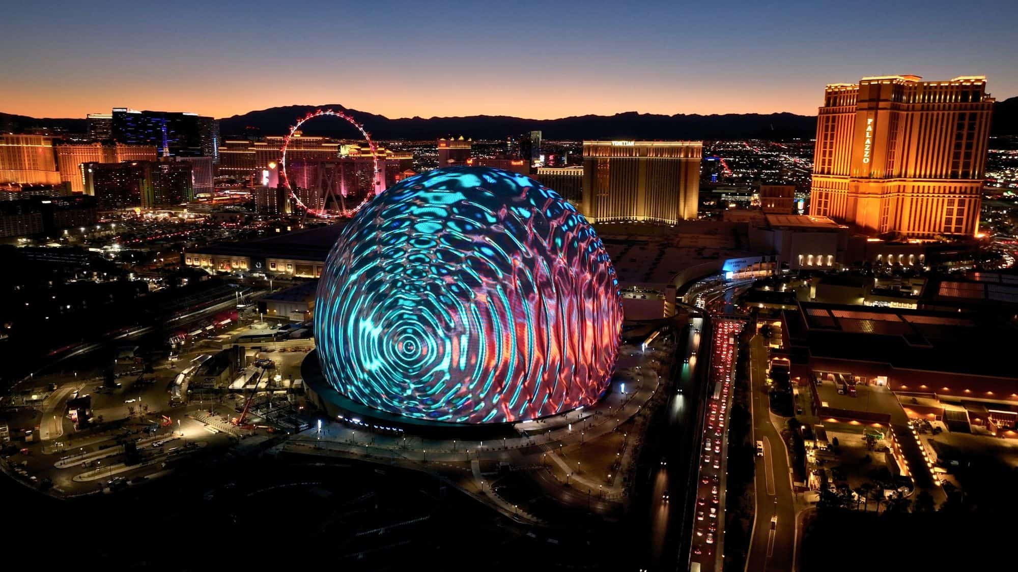 The futuristic Sphere in Las Vegas illuminates the night sky with swirling digital patterns, surrounded by the dazzling lights of the Las Vegas Strip. The nearby High Roller Ferris wheel and city skyline create an electrifying backdrop.