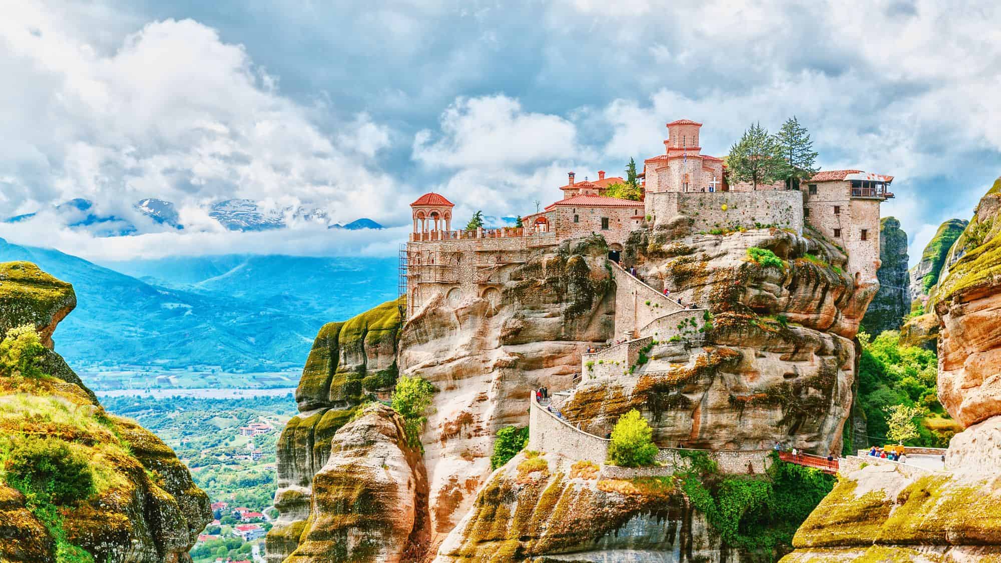The breathtaking Meteora monasteries sit atop towering rock formations, with a misty mountain landscape in the background, creating an almost otherworldly view.