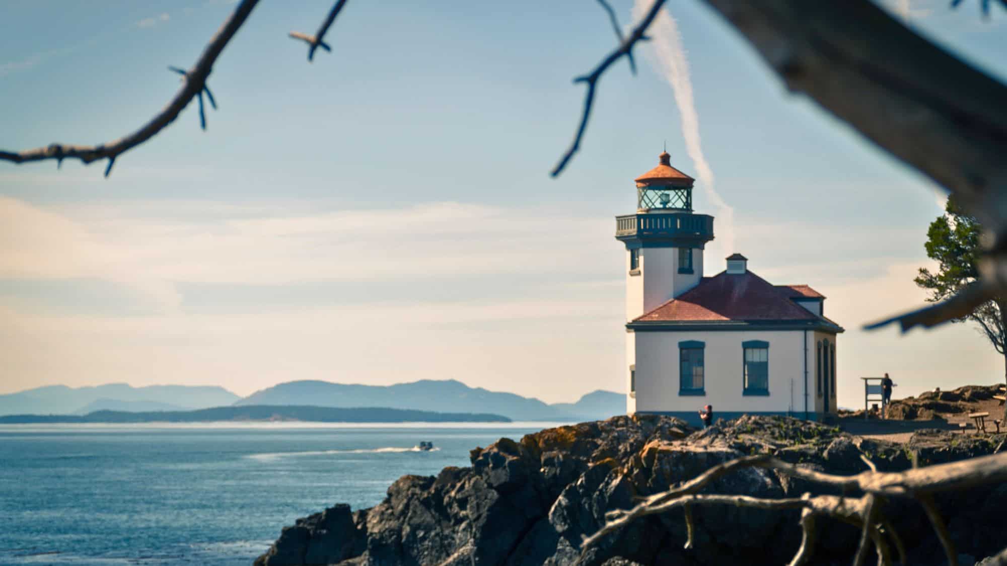 A charming lighthouse perched on a rocky coastline, overlooking the calm blue waters. The soft light and distant mountains in the background enhance the tranquil setting.