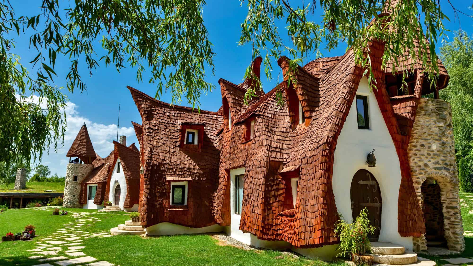 A whimsical fairytale-like cottage with curved rooftops and earthy tones is nestled among lush greenery in Sibiu, Romania, creating a magical atmosphere.