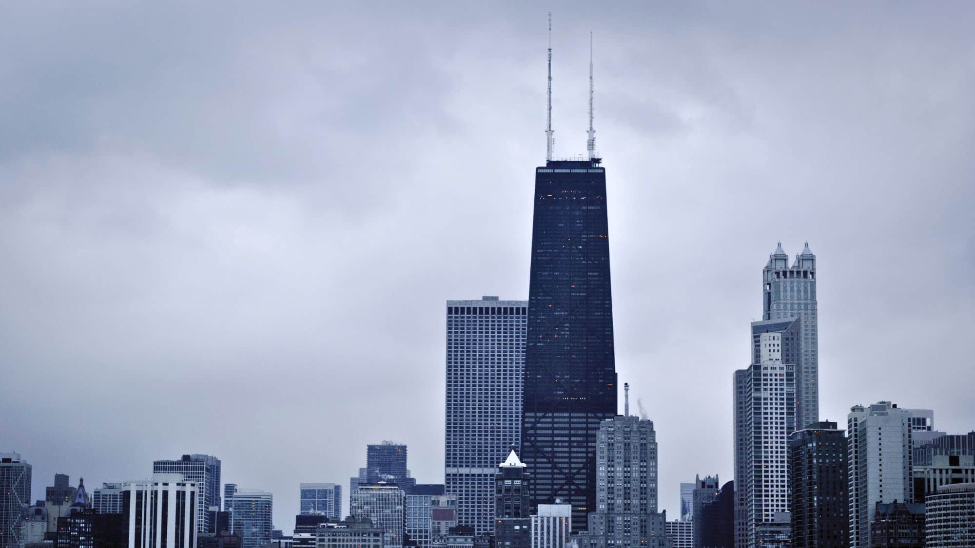 A moody, overcast view of the Willis Tower (formerly Sears Tower) dominating the Chicago skyline. The dark glass facade and twin antennae give the skyscraper a commanding presence among surrounding high-rises.