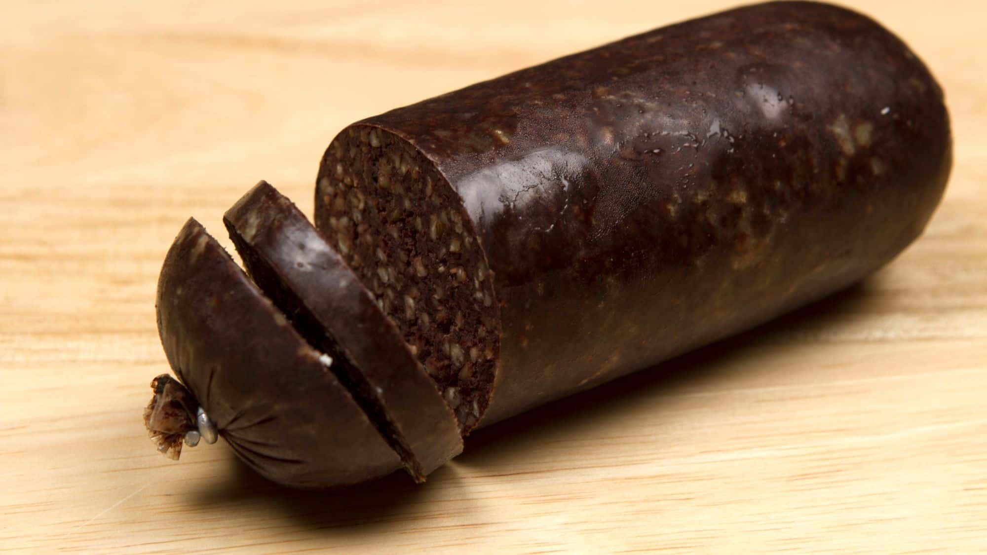 A dark, thick slice of black pudding, a traditional blood sausage made with pork blood and oats, served on a wooden board with a rustic presentation.