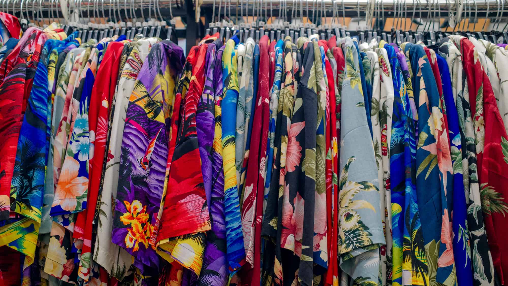 A row of vibrant Hawaiian shirts in various colors and floral patterns hangs neatly on a clothing rack, creating a bold and tropical display.