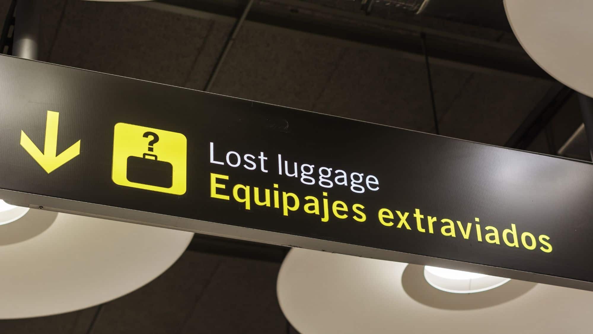 A black and yellow airport sign reads "Lost luggage / Equipajes extraviados," directing travelers to the baggage claim assistance area.