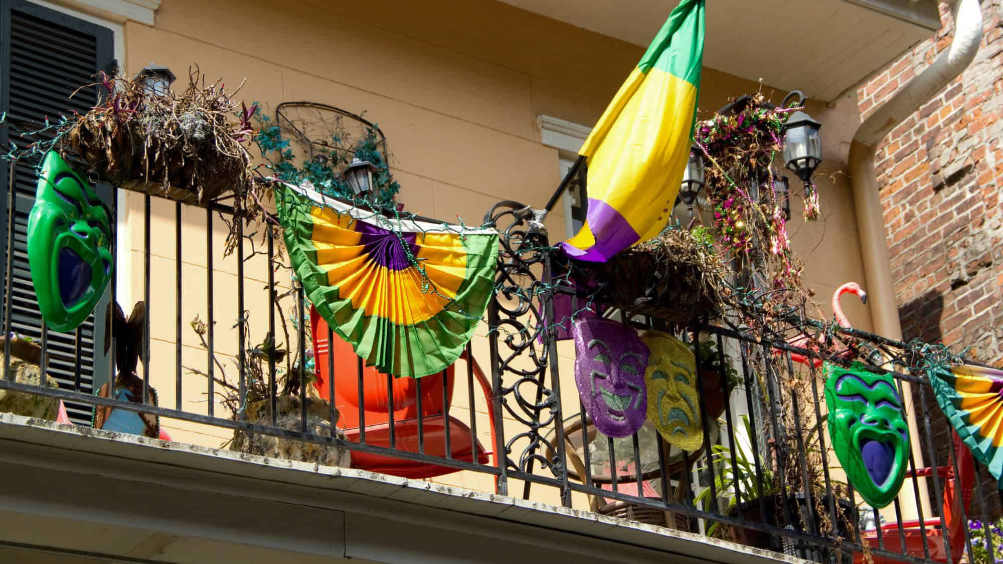 A festive balcony in New Orleans, decorated with colorful Mardi Gras masks, garlands, and the signature purple, green, and gold flag.