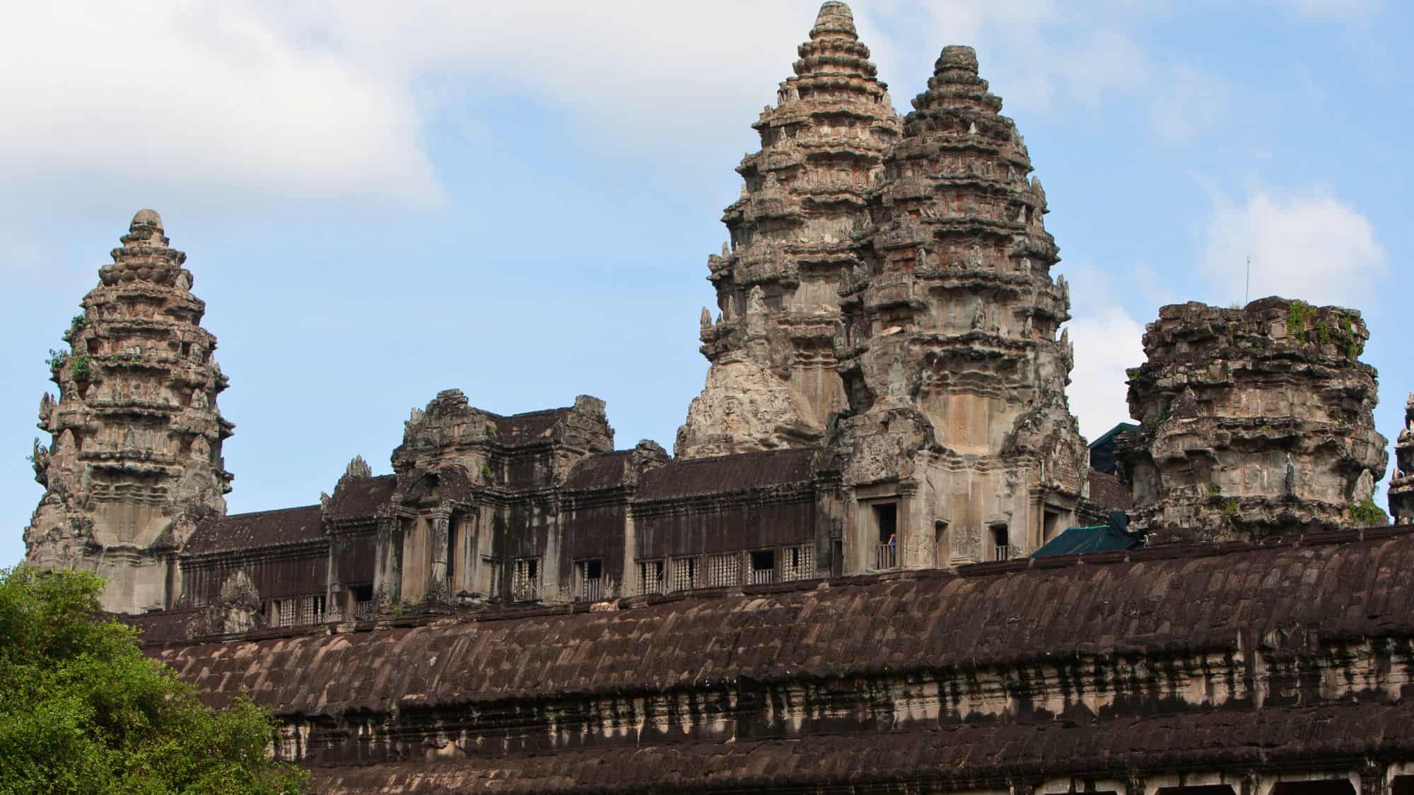 Close-up view of the ornate stone towers of Angkor Wat in Cambodia, with intricate carvings and weathered stonework under a partly cloudy sky.