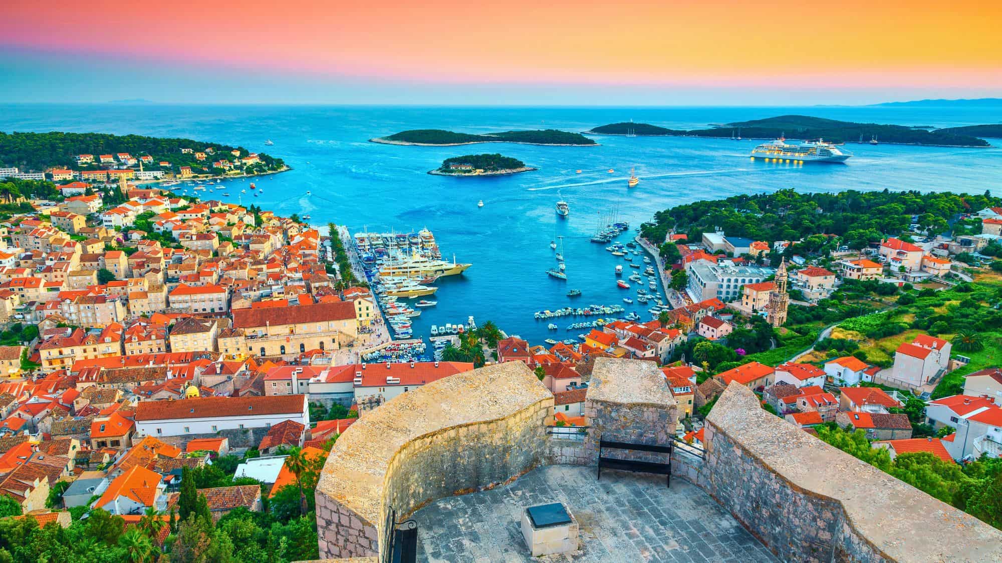 Overlook from the Fortress Spanjola in Herceg Novi, Montenegro, showing colorful sunset skies over a marina filled with yachts and a terracotta-roofed coastal town.