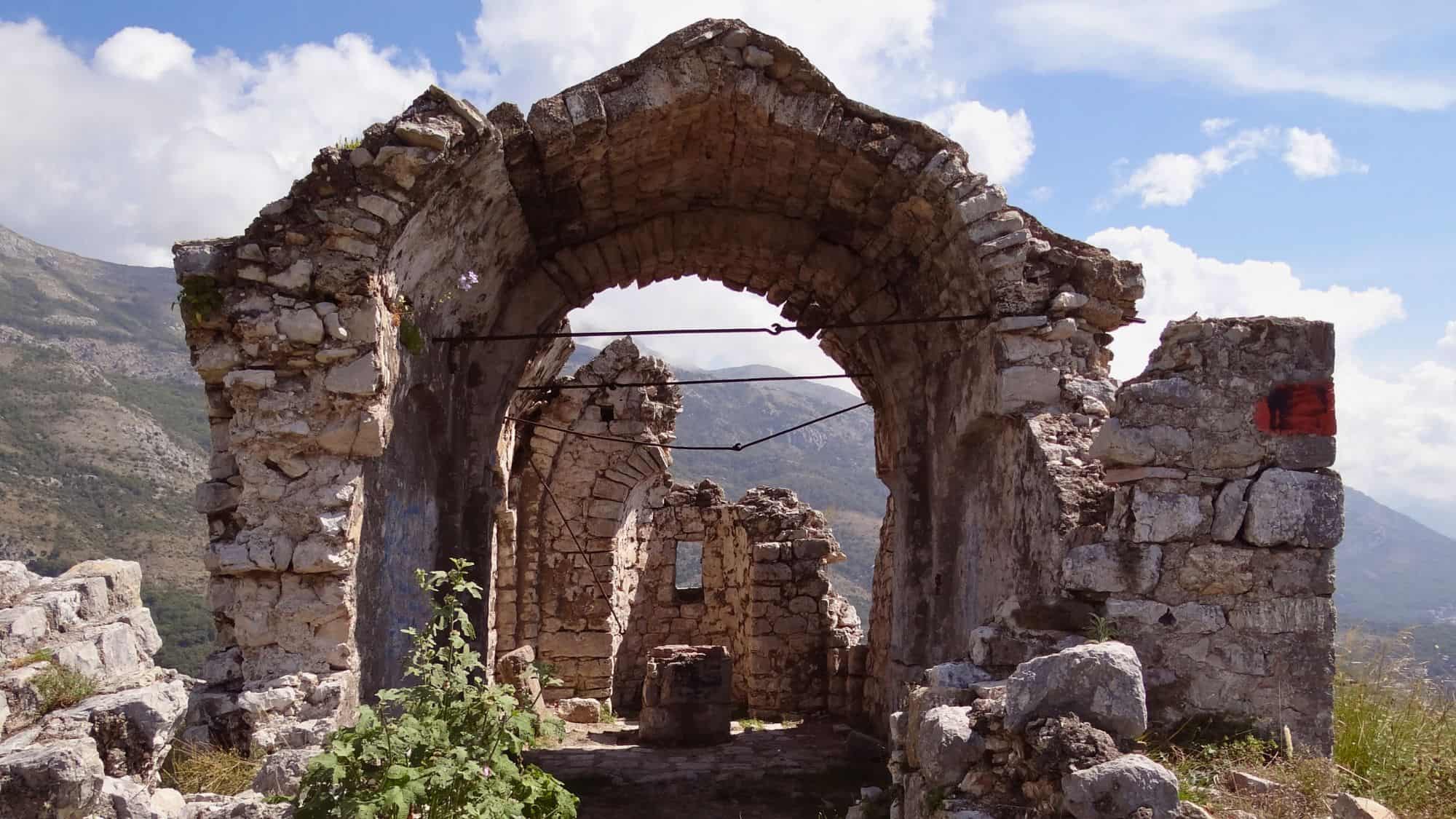 Rugged ruins of Haj Nehaj Fortress in Montenegro perched atop a mountain, with arched stone remnants and open window views into the valleys below.