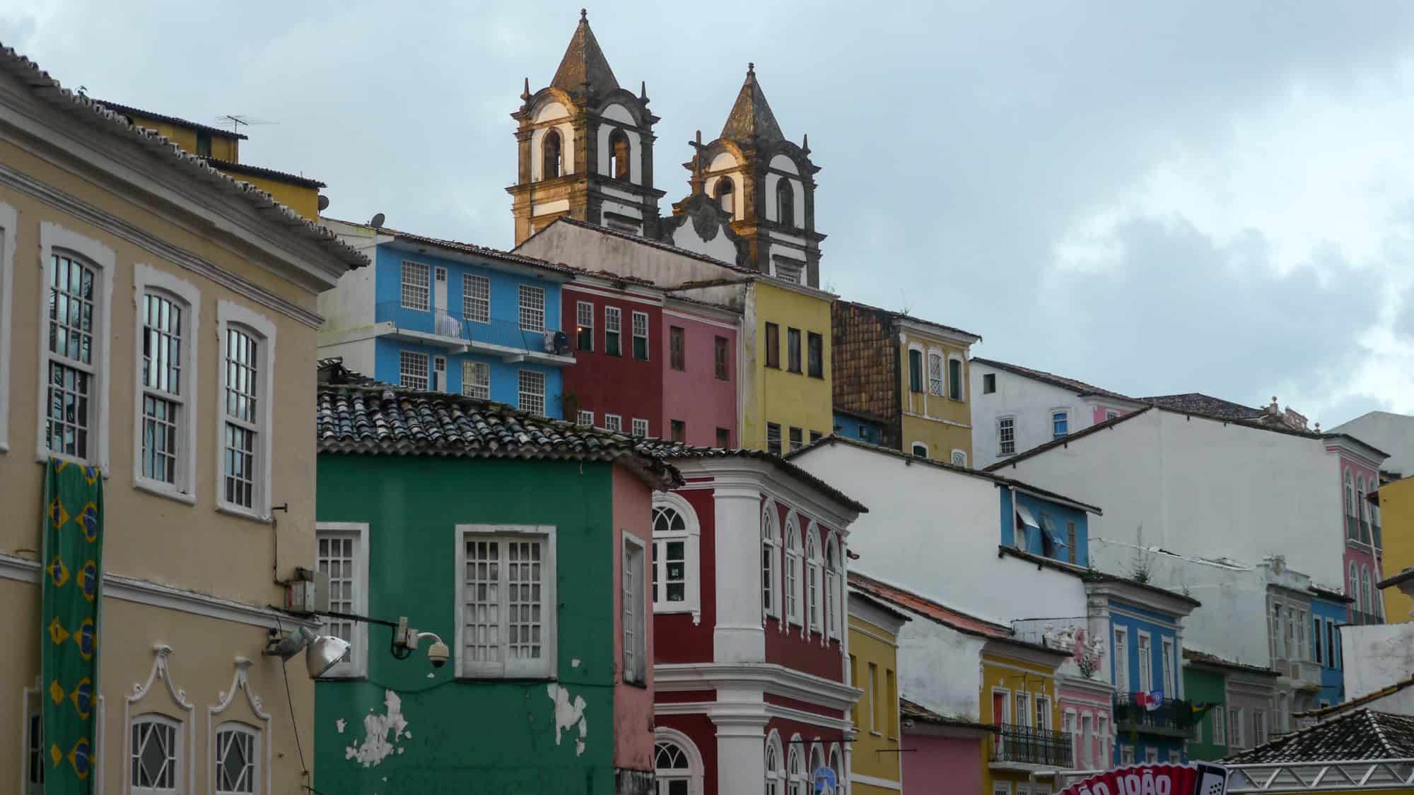 A colorful row of colonial buildings in Salvador’s historic center, with pastel-painted facades and twin church towers rising above the tightly packed homes.