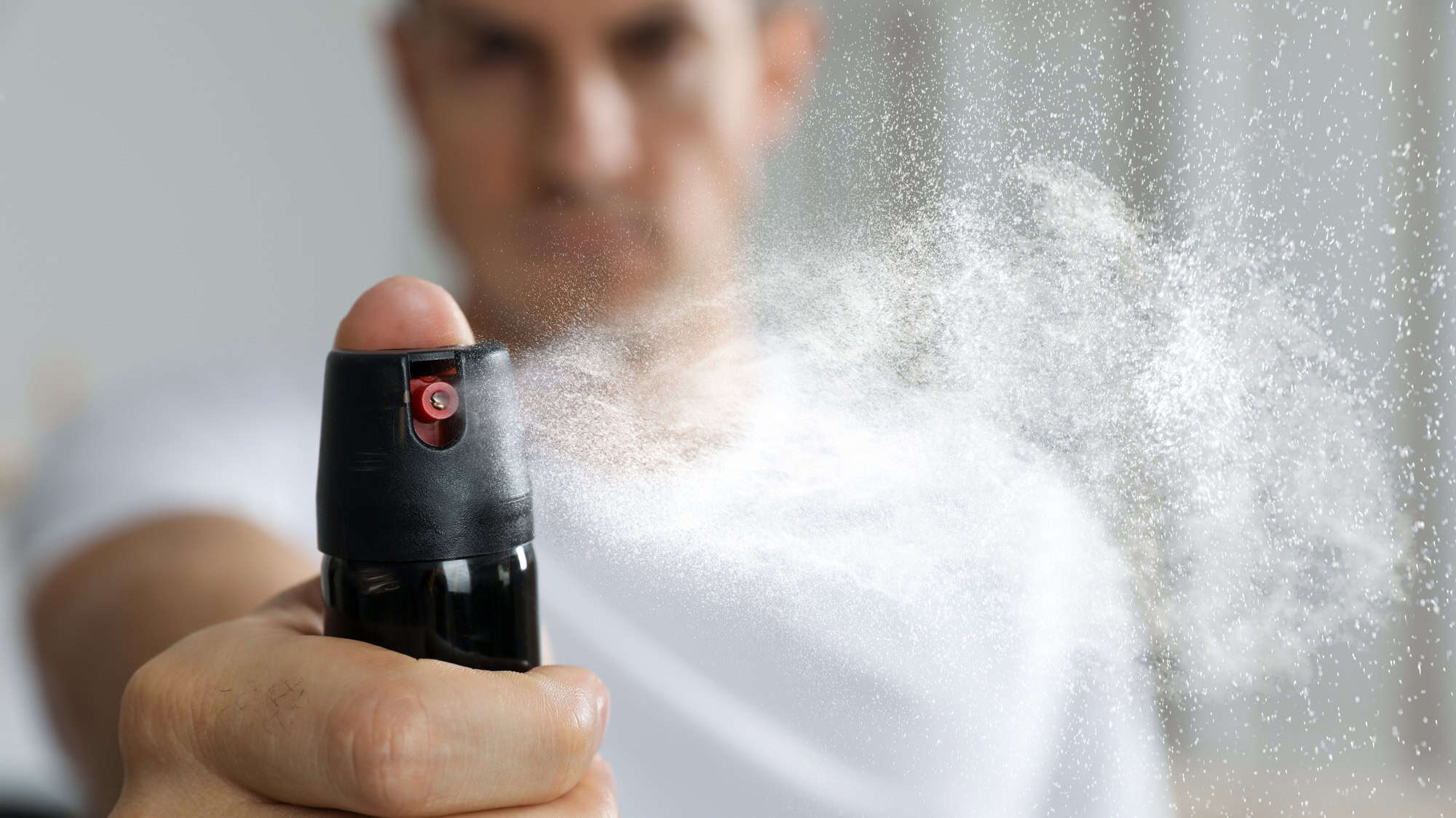 A close-up view of a man using pepper spray, showing a powerful mist spraying forward as he holds the canister with firm intent.