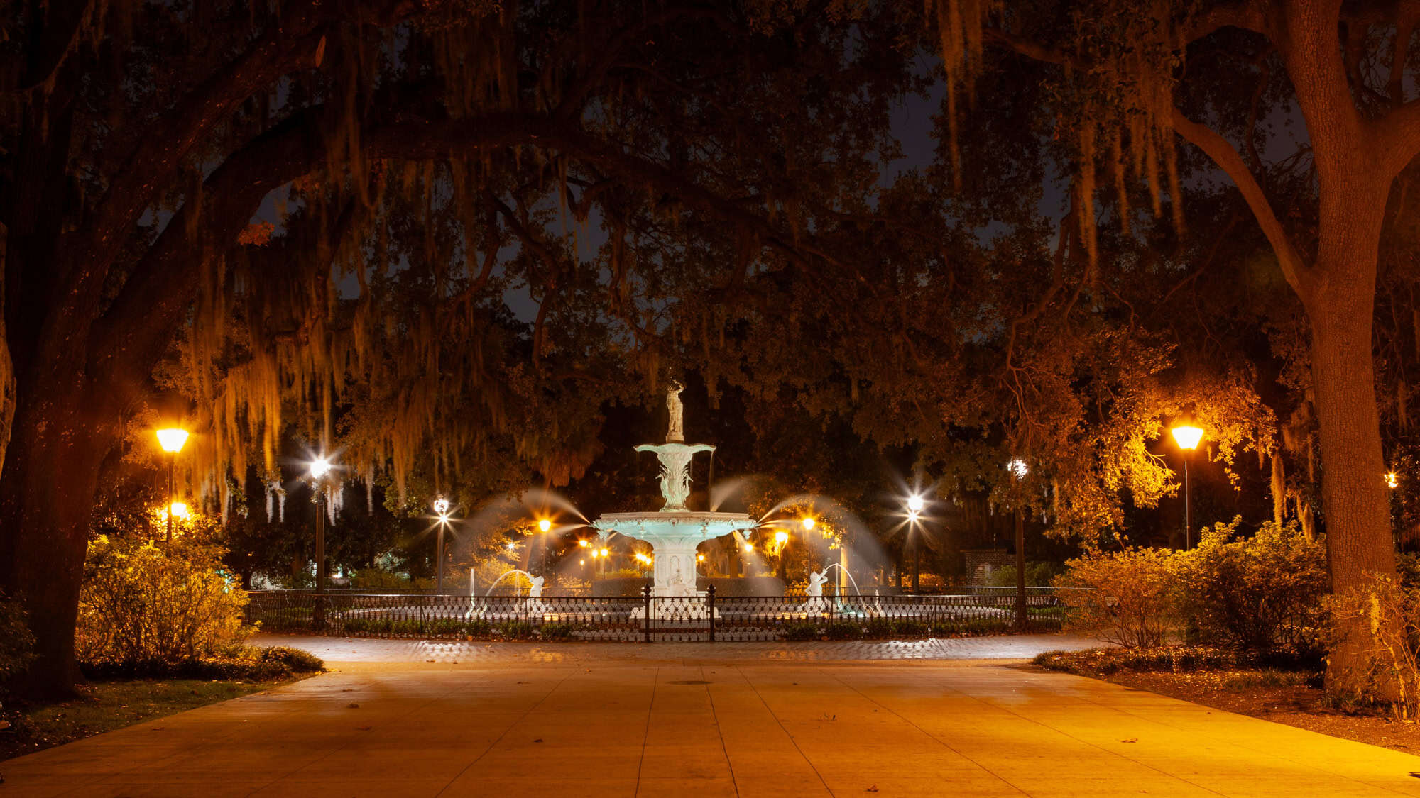 Glowing fountain in Savannah’s Forsyth Park lit up at night, surrounded by moss-draped oaks and warmly lit pathways.
