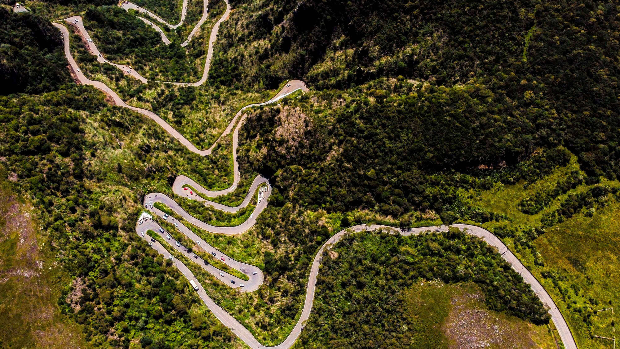 Aerial view of Brazil’s iconic Serra do Rio do Rastro Road, with hairpin turns zigzagging through a lush, mountainous landscape covered in dense forest.