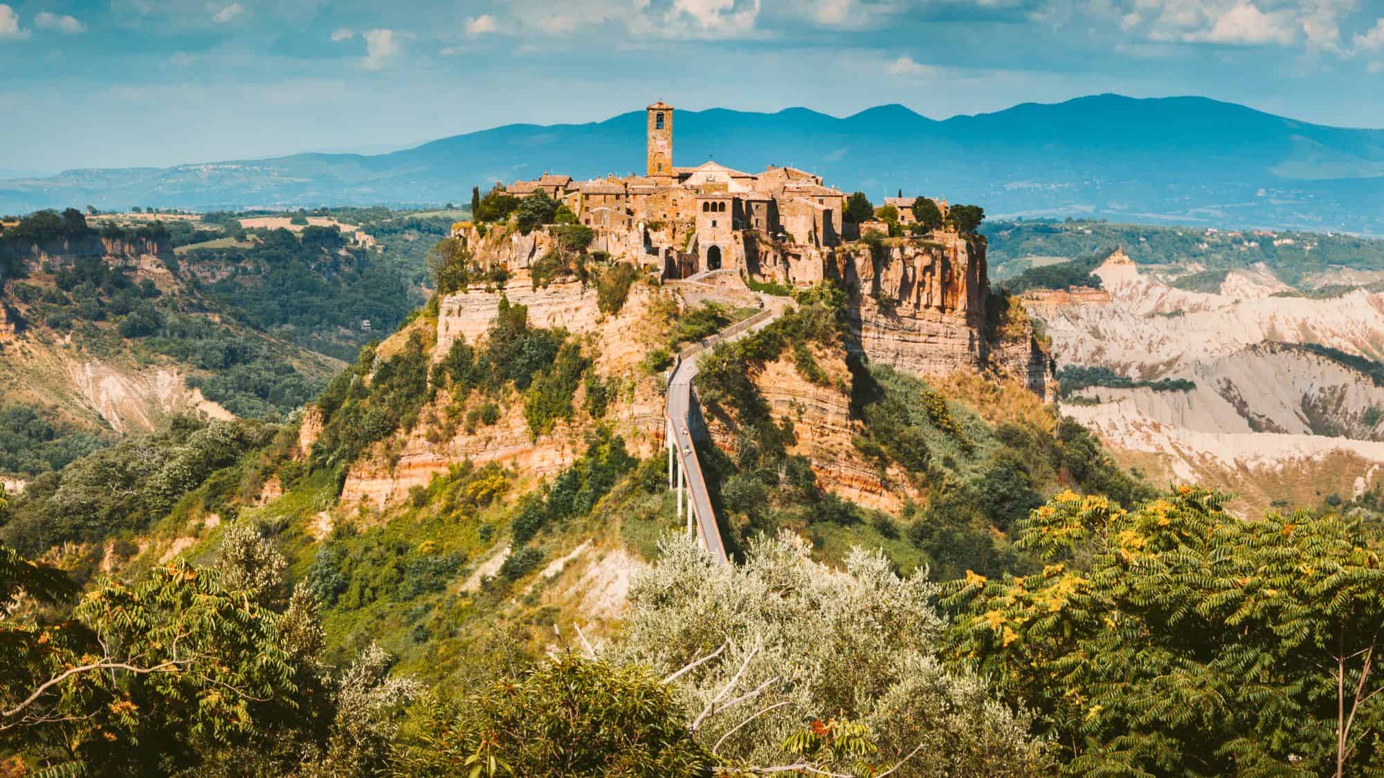 A medieval hilltop town in central Italy, dramatically perched on a plateau of crumbling volcanic rock, accessed by a long pedestrian bridge.