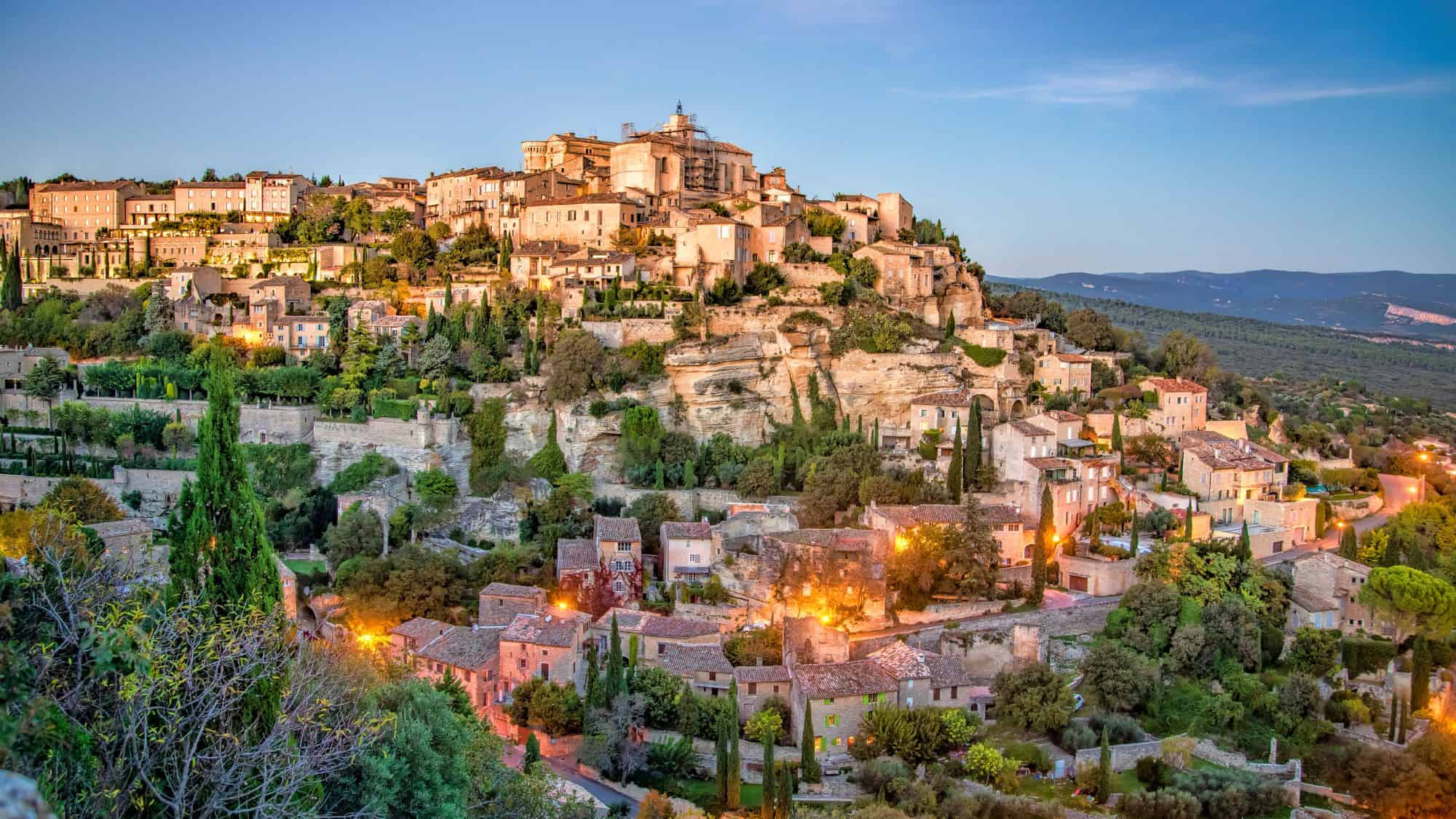 A stunning hilltop village in Provence, with stone houses cascading down the slope, bathed in the warm glow of sunset lights.