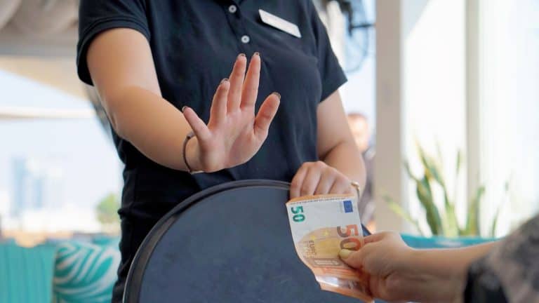 A server in a black uniform raises her hand to politely decline a 50-euro tip being offered by a customer, capturing a moment of cultural or personal refusal of gratuity.