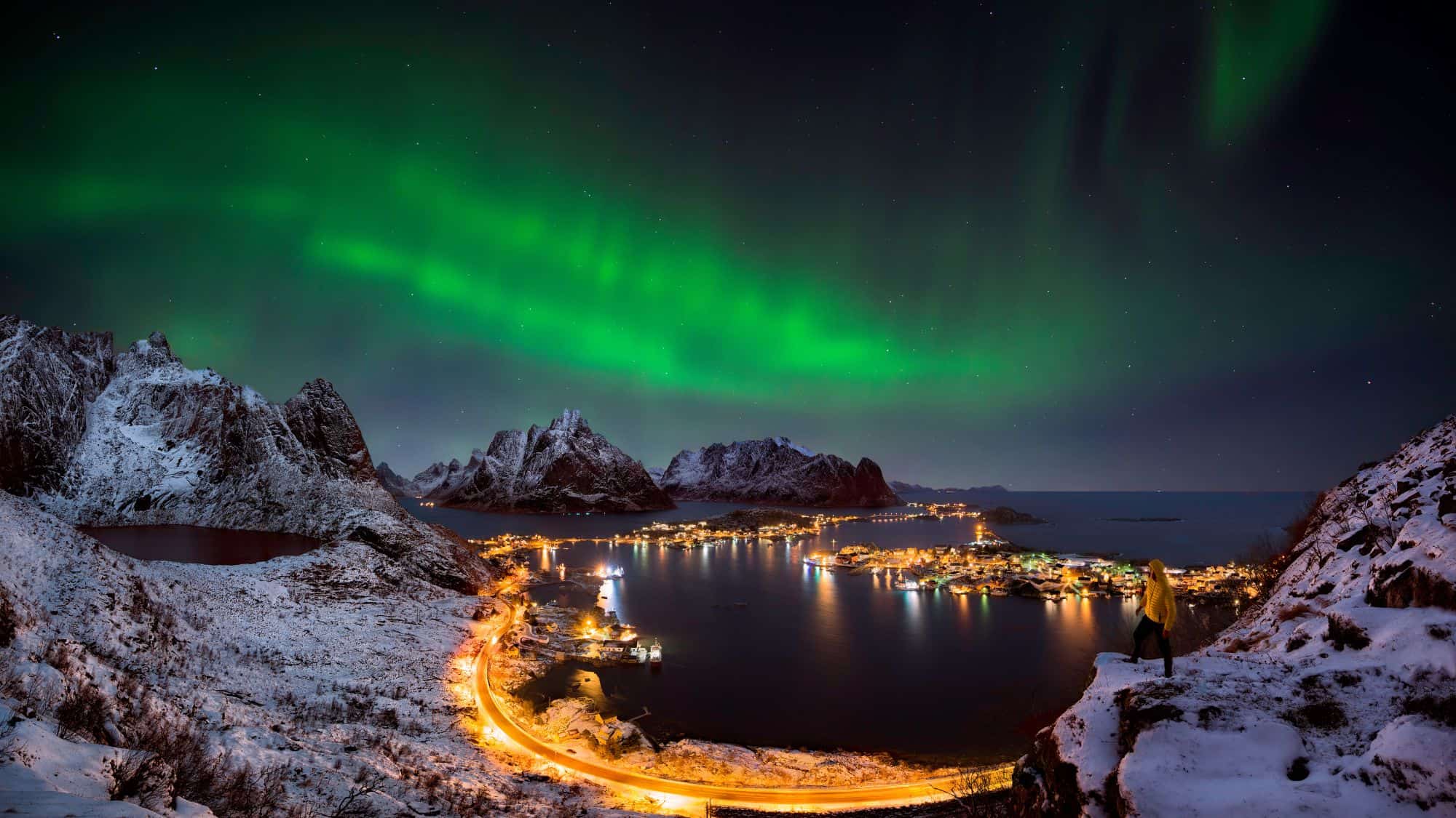 A breathtaking Arctic village under the glowing northern lights, with snow-covered mountains, fjords, and twinkling village lights.