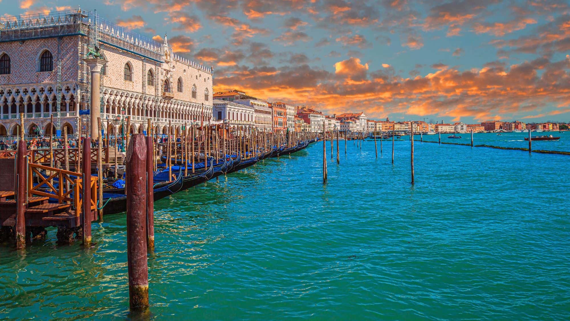 VENICE, ITALY - MARCH 16, 2023: View along the Riva degli Schiavoni, with the Doges' Palace, traditional Venetian architecture, boats, gondolas and the sea. Sunset light.