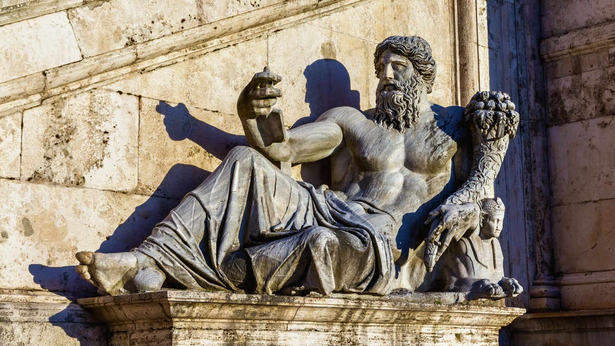 A stone statue of a reclining bearded man holding a scroll and a cornucopia, known as Marforio, sits at the base of a staircase in Rome, symbolizing one of the city's “talking statues.”
