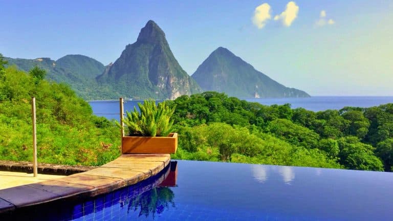 The iconic twin peaks of the Pitons rise dramatically from the sea, seen from an infinity pool with tropical foliage in the foreground.
