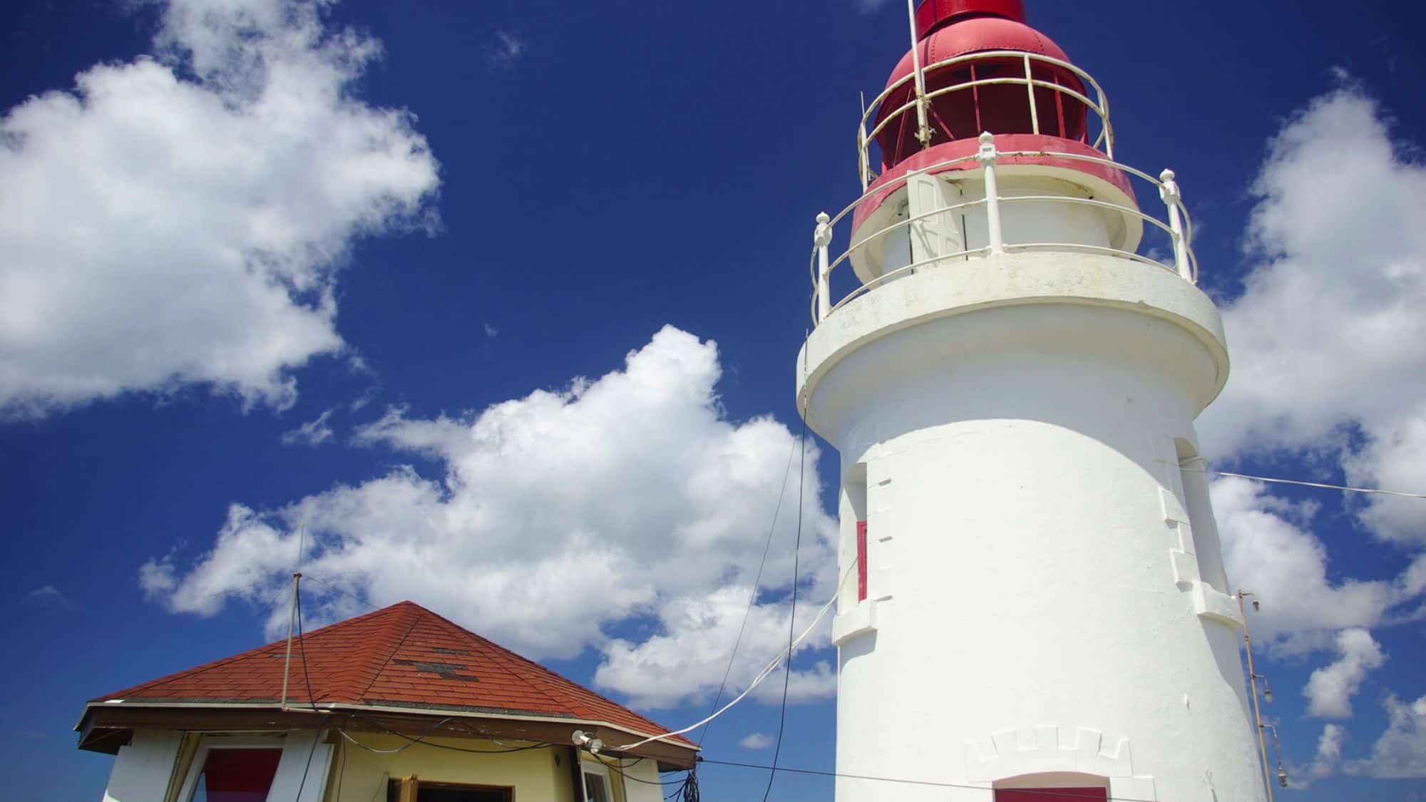 Close-up view of the white and red Vigie Lighthouse in St. Lucia, set against a bright blue sky with scattered white clouds.