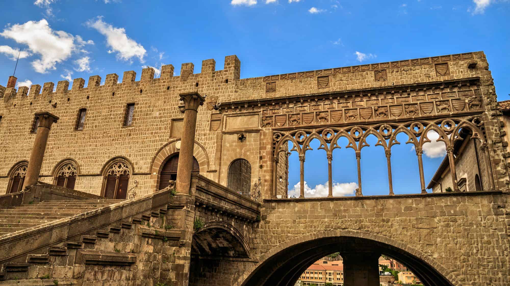 A detailed view of Viterbo’s Palazzo dei Papi, showcasing its crenellated stone walls, arched staircase, and Gothic loggia with sculpted designs.