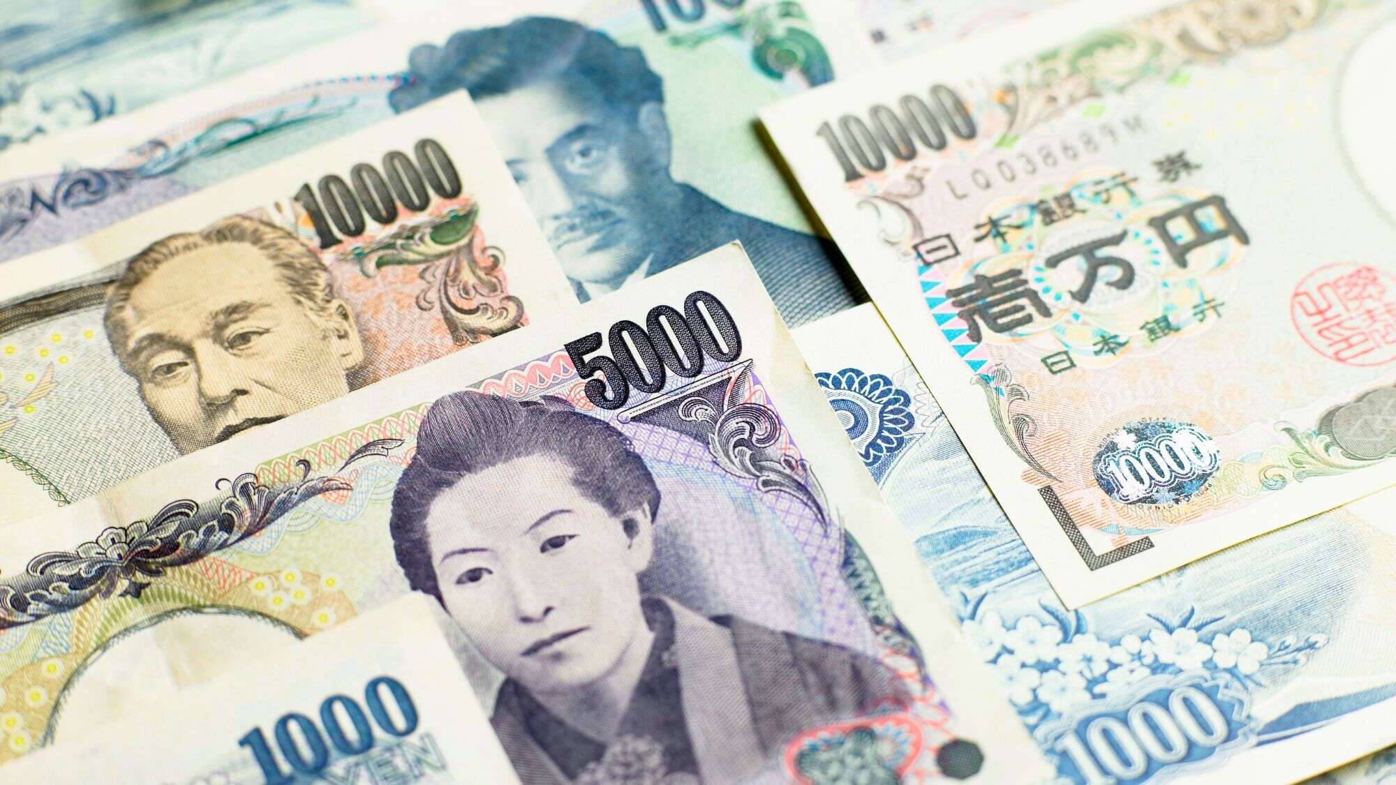 A spread of colorful Japanese yen banknotes, including denominations of 1,000, 5,000, and 10,000 yen, featuring traditional portraits and intricate patterns in blue, purple, and beige tones.