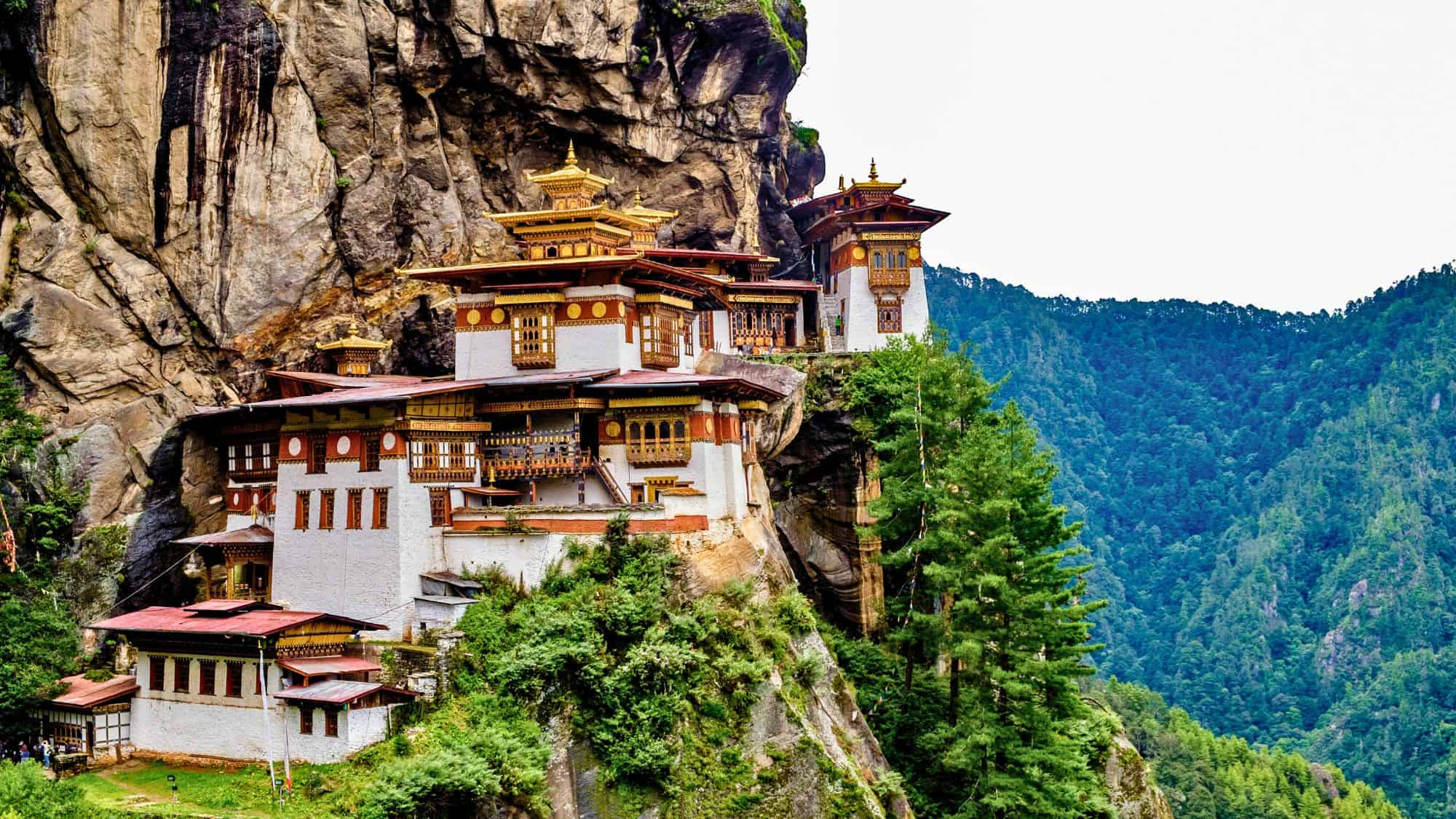 The iconic Paro Taktsang monastery, also known as the Tiger’s Nest, clings dramatically to a cliffside above a lush forested valley in Bhutan.