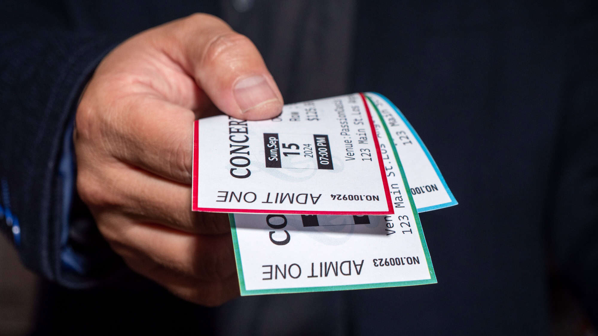 A hand holds out several concert tickets, clearly showing event details including a 7:00 PM start time and venue address on Main Street.