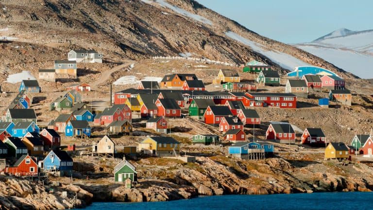 A closer and more concentrated view of colorful red, blue, green, and yellow houses packed together on a rocky slope with patches of snow and ice, surrounded by a dramatic Arctic landscape.