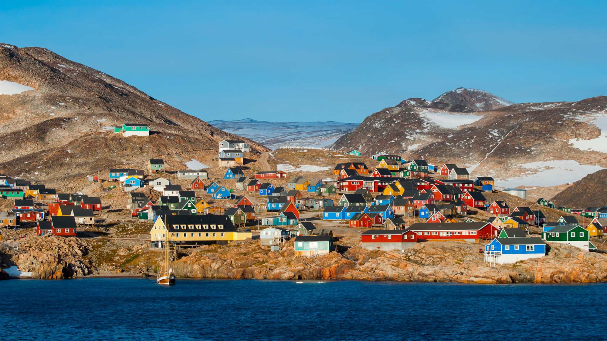 A remote settlement with vibrantly painted houses scattered across rocky terrain, nestled between snow-dusted hills and Arctic waters.