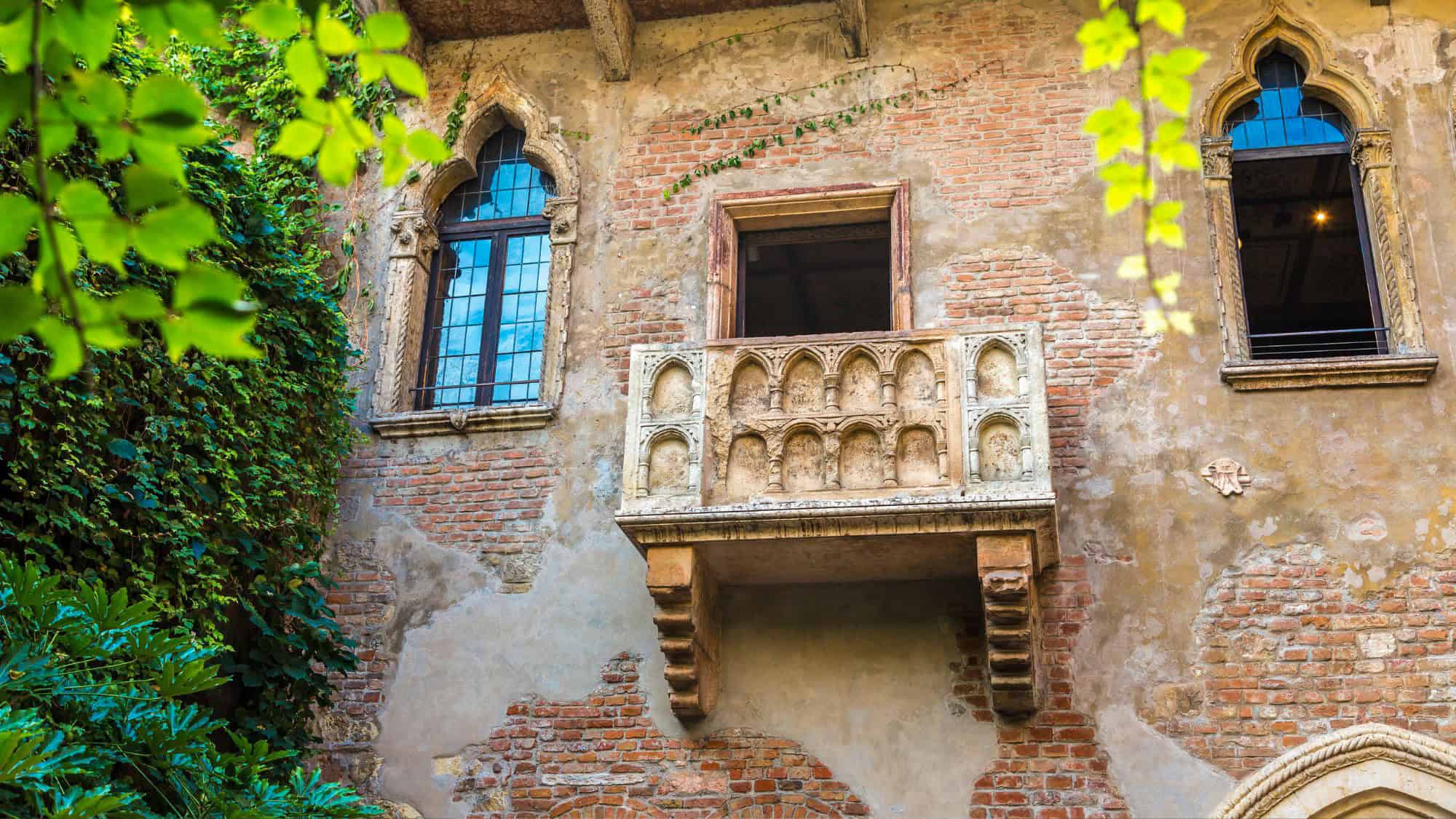 An ornate stone balcony juts out from a brick facade covered in ivy at Casa di Giulietta in Verona, Italy. The site is famously linked to Shakespeare’s Romeo and Juliet and attracts romantic visitors from around the world.