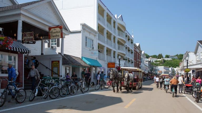 Mackinac Island downtown filled with people and a horse drawn carriage coming down the road.