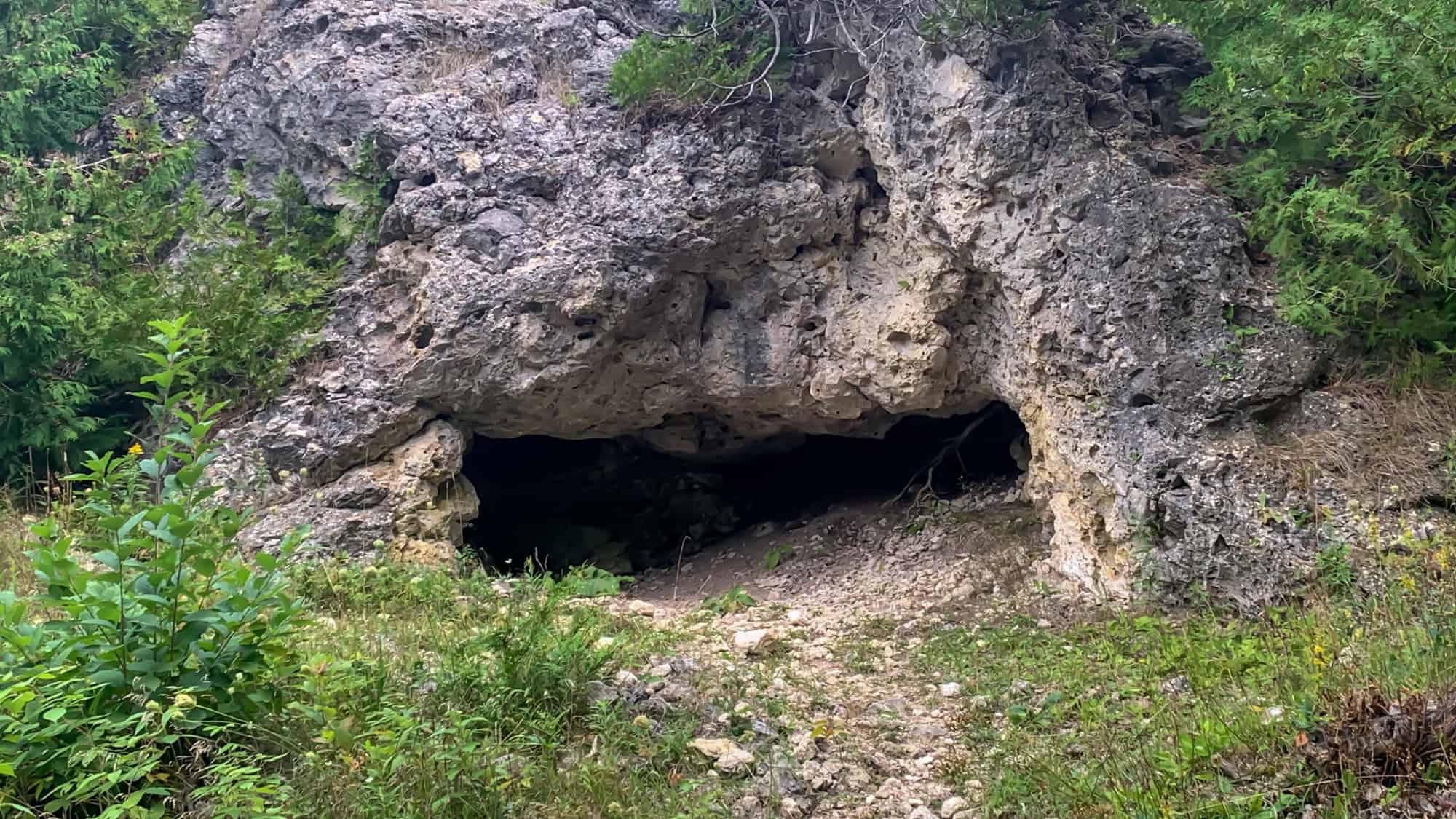 Low, wide entrance to Skull Cave, a shallow limestone cavern surrounded by greenery, partially hidden in the natural rock of Mackinac Island.