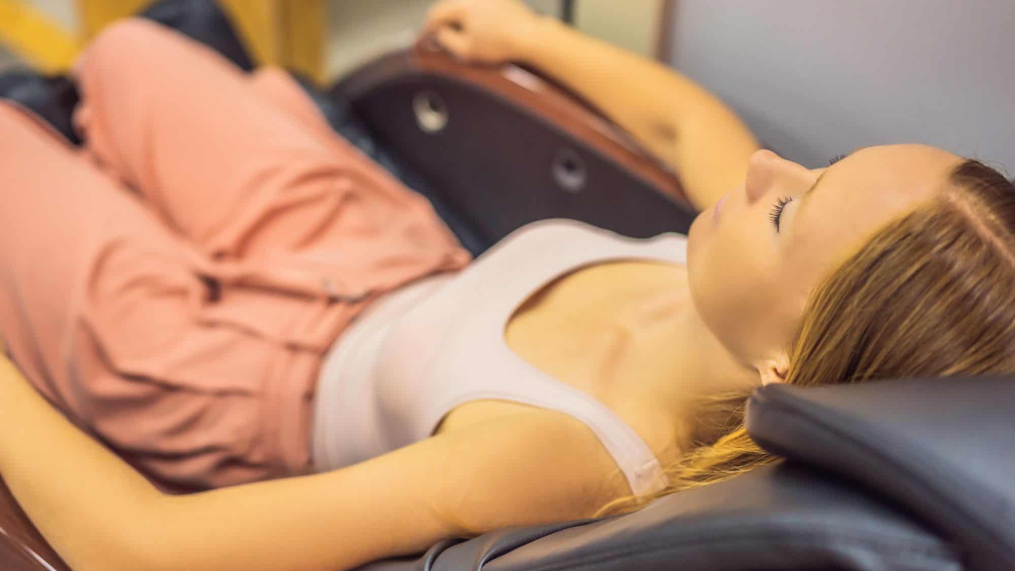 Close-up view of a woman reclining with her eyes closed in a padded massage chair, showcasing airport comfort amenities during travel.