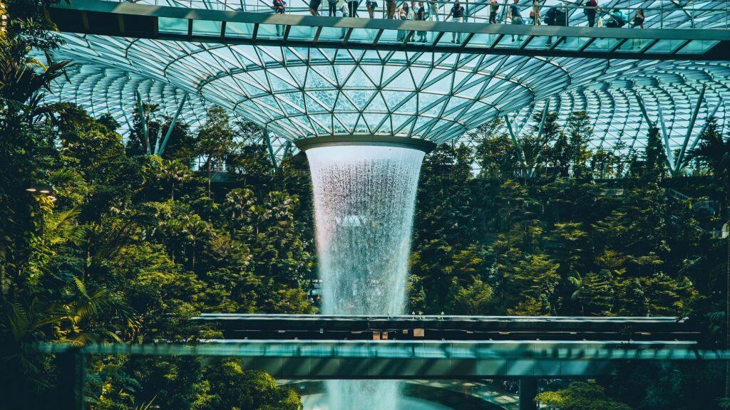 Singapore Changi Airport’s Jewel complex showcases the world’s tallest indoor waterfall, the Rain Vortex, surrounded by lush indoor forest vegetation and an elevated walkway beneath a glass dome ceiling.