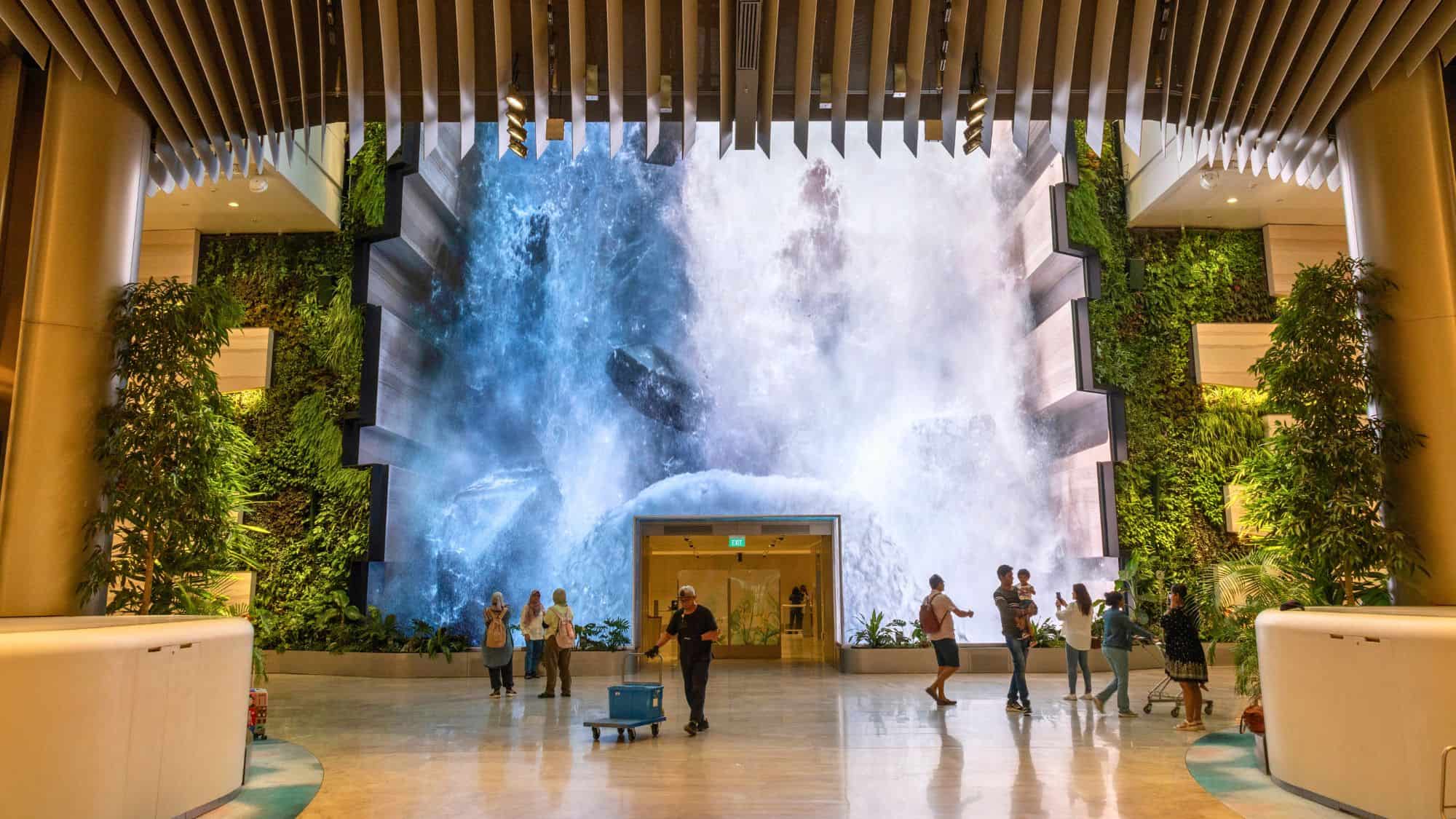 A jaw-dropping digital waterfall display cascades down a massive screen surrounded by lush vertical greenery, creating an immersive environment for airport visitors.