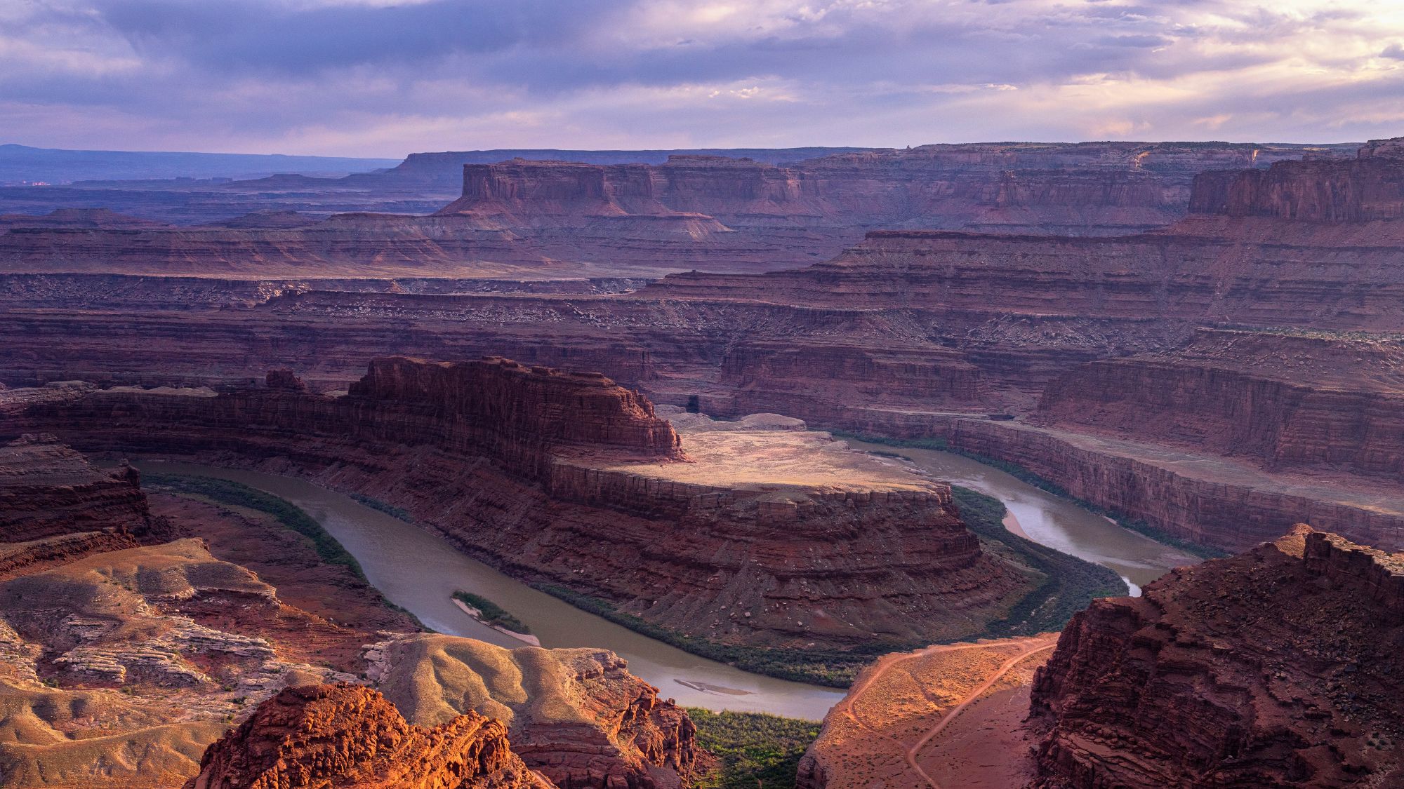 A dramatic overlook of Dead Horse Point State Park, with layered red rock canyons and a winding river carving through the desert at sunset.