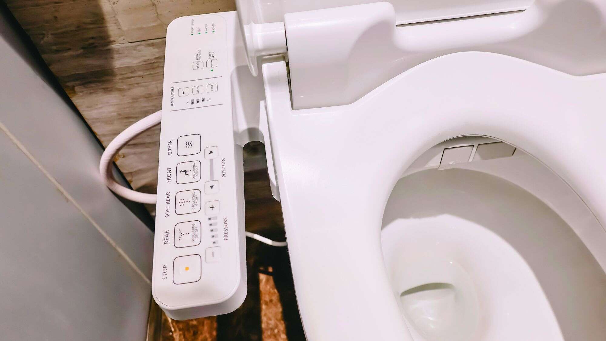 Modern Japanese toilet with an attached control panel featuring multiple buttons for spray types, seat temperature, and dryer functions.