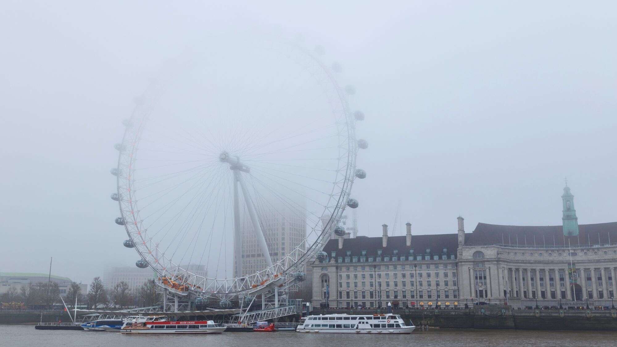 The London Eye is barely visible as dense fog engulfs the famous Ferris wheel along the Thames, softening the cityscape and blurring architectural lines.