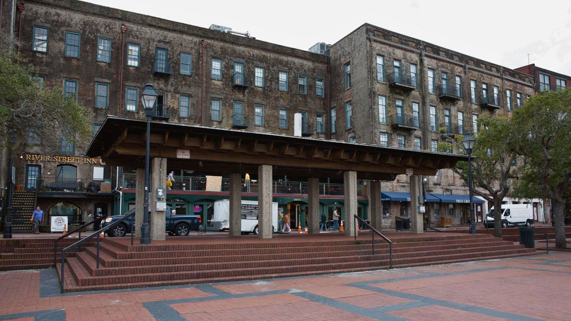 A view of Savannah’s Plant Riverside District with weathered brick buildings, shopfronts, and a wide plaza in front of River Street Inn, blending historic charm with modern retail.