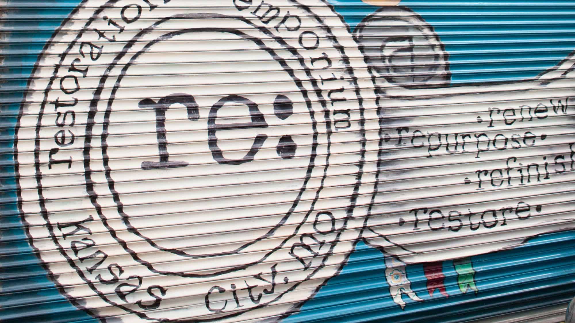 A painted sign on a blue roll-up door in Kansas City that reads “re: Restoration Emporium,” with additional words like “renew,” “repurpose,” “refinish,” and “restore” in hand-lettered style.