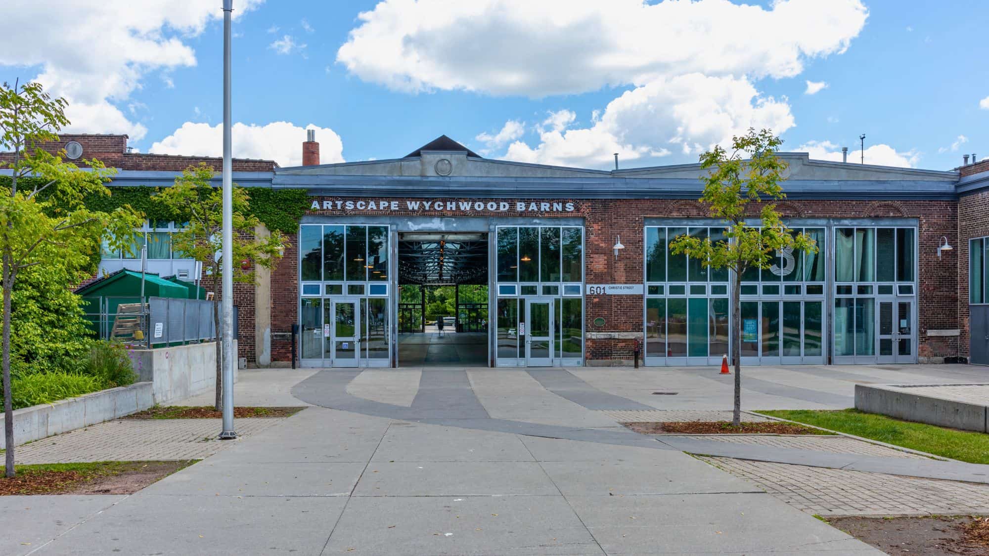 Exterior of Artscape Wychwood Barns in Toronto, featuring glass-paneled doors, brick walls with ivy, and an inviting open plaza leading into a repurposed industrial community hub.